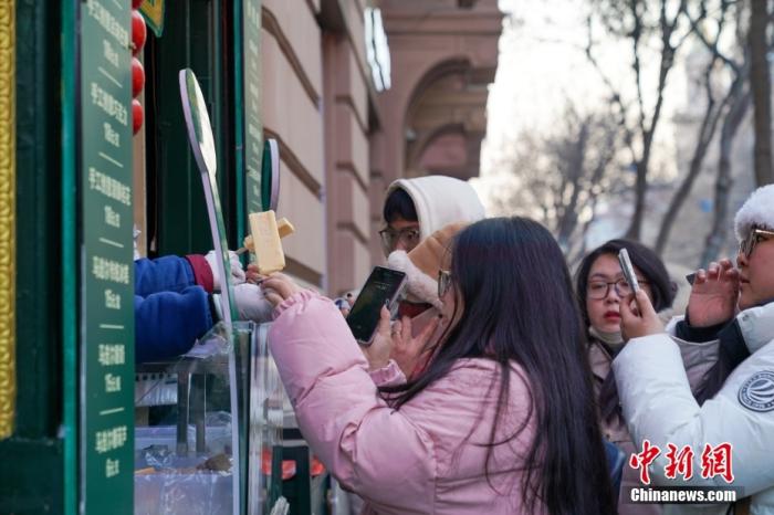 资料图：1月2日，在黑龙江哈尔滨中央大街，游客身着厚衣服在寒冷的天气中品尝雪糕，手拿雪糕拍照，成为哈尔滨冬日一景。 <a target='_blank' href='/'>中新社</a>发 赵宇航 摄